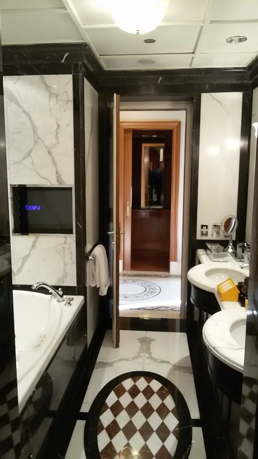 Bagno rivestito in marmo con vasca, doccia e pavimento a scacchi